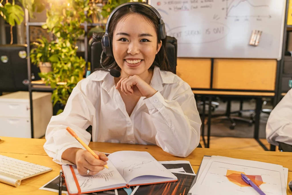 Femme souriante avec casque micro travaillant sur des graphiques dans un bureau.