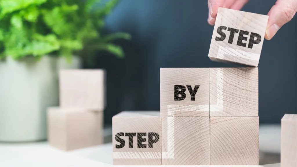Main empilant des blocs en bois gravés des mots “Step by Step” dans un concept de progression.