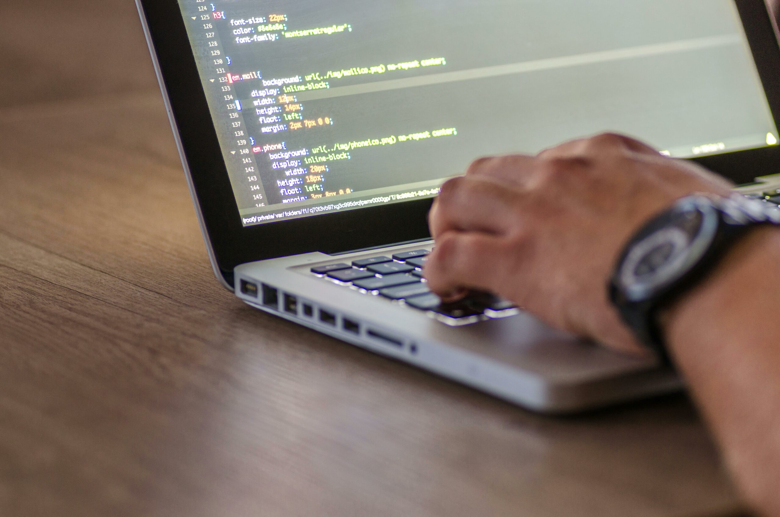 Main tapant sur un clavier d’ordinateur portable affichant du code source.