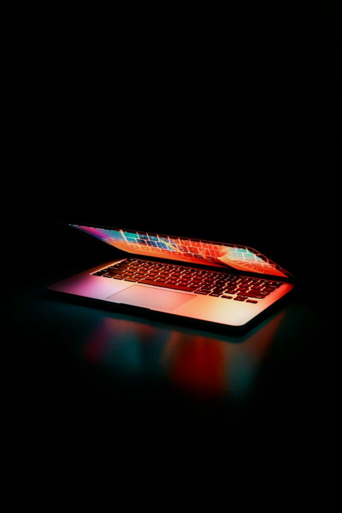 Ordinateur portable à moitié ouvert illuminé par des lumières colorées dans l’obscurité.
