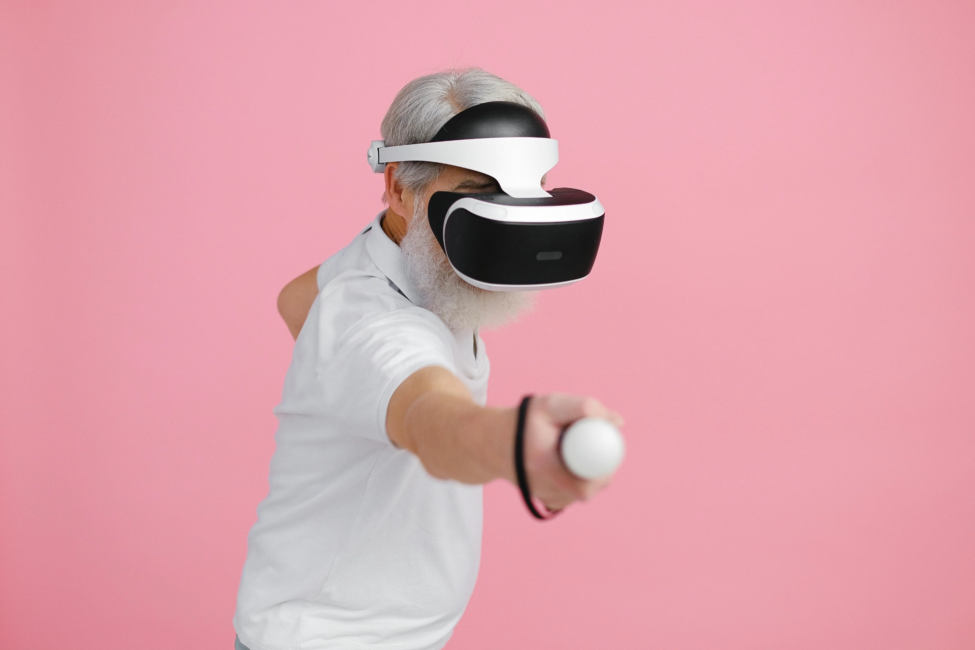 Homme âgé utilisant un casque de réalité virtuelle et une manette sur fond rose.