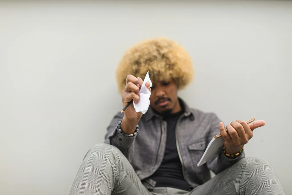 Une personne assise, froissant une feuille de papier avec un crayon dans l'autre main.