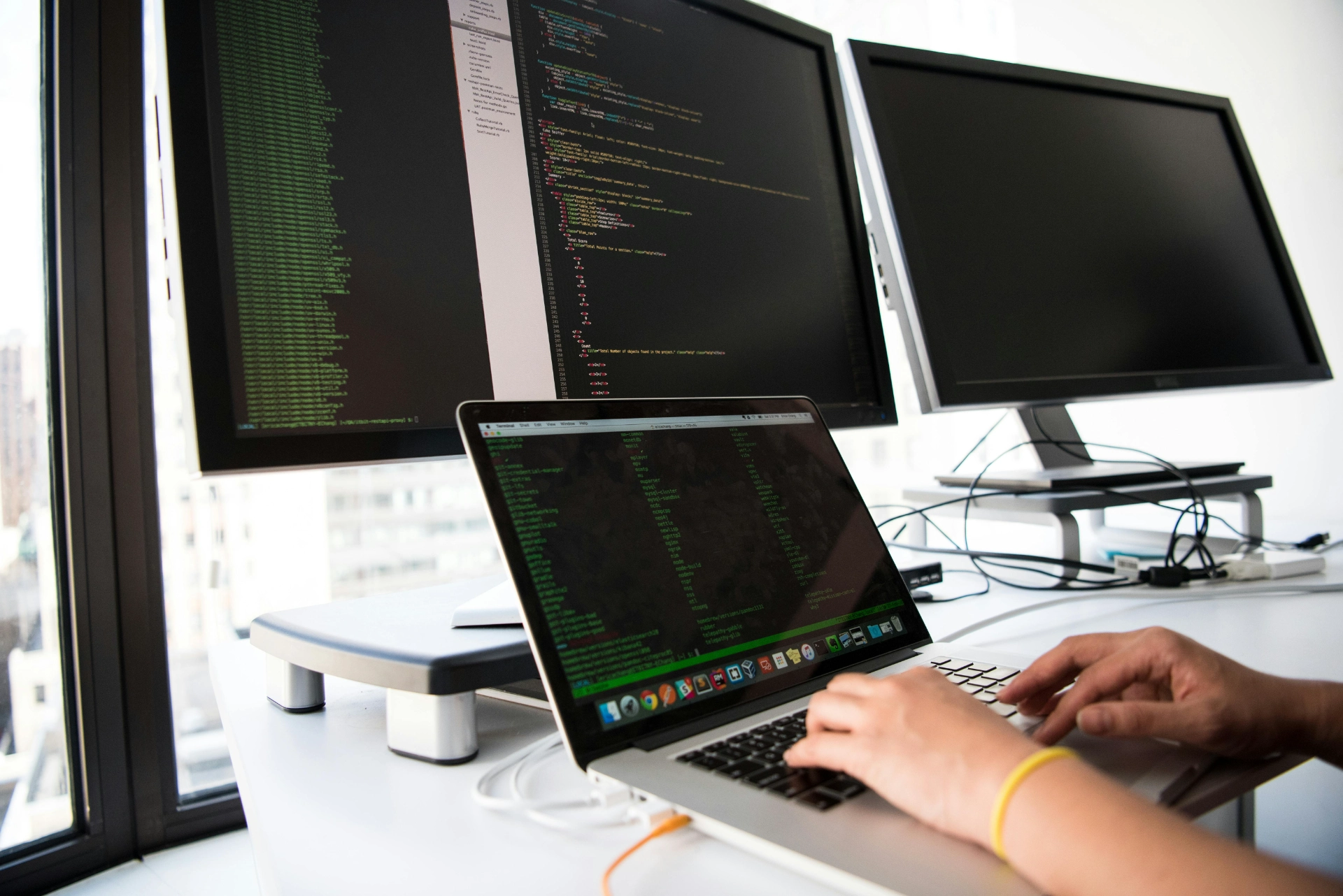 Personne tapant du code sur un ordinateur portable avec plusieurs écrans affichant du code.