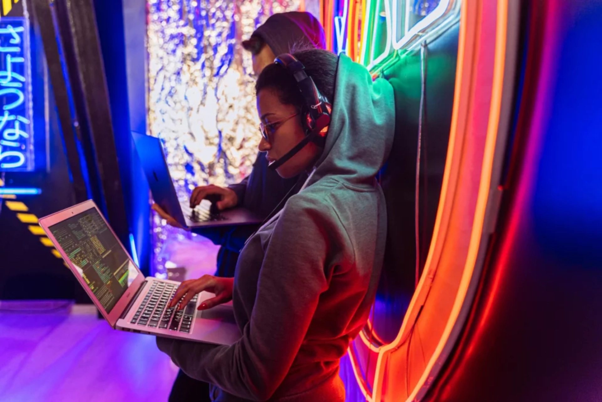 Jeunes informaticiens en hoodie codant sur des ordinateurs portables dans une ambiance néon.