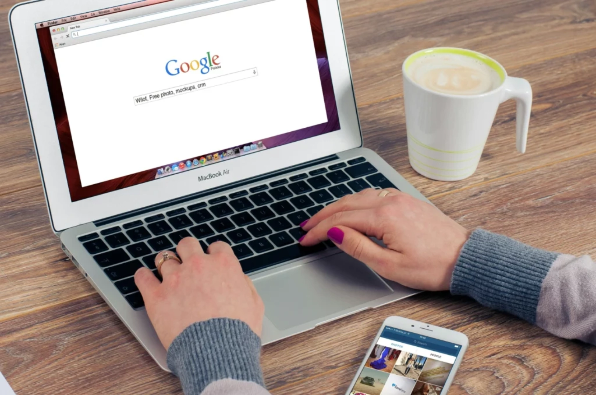 Personne effectuant une recherche sur Google sur un MacBook Air, avec un smartphone et un café à côté.