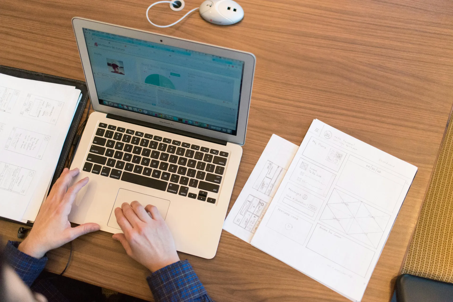Utilisateur travaillant sur un ordinateur portable avec des wireframes papier sur un bureau.
