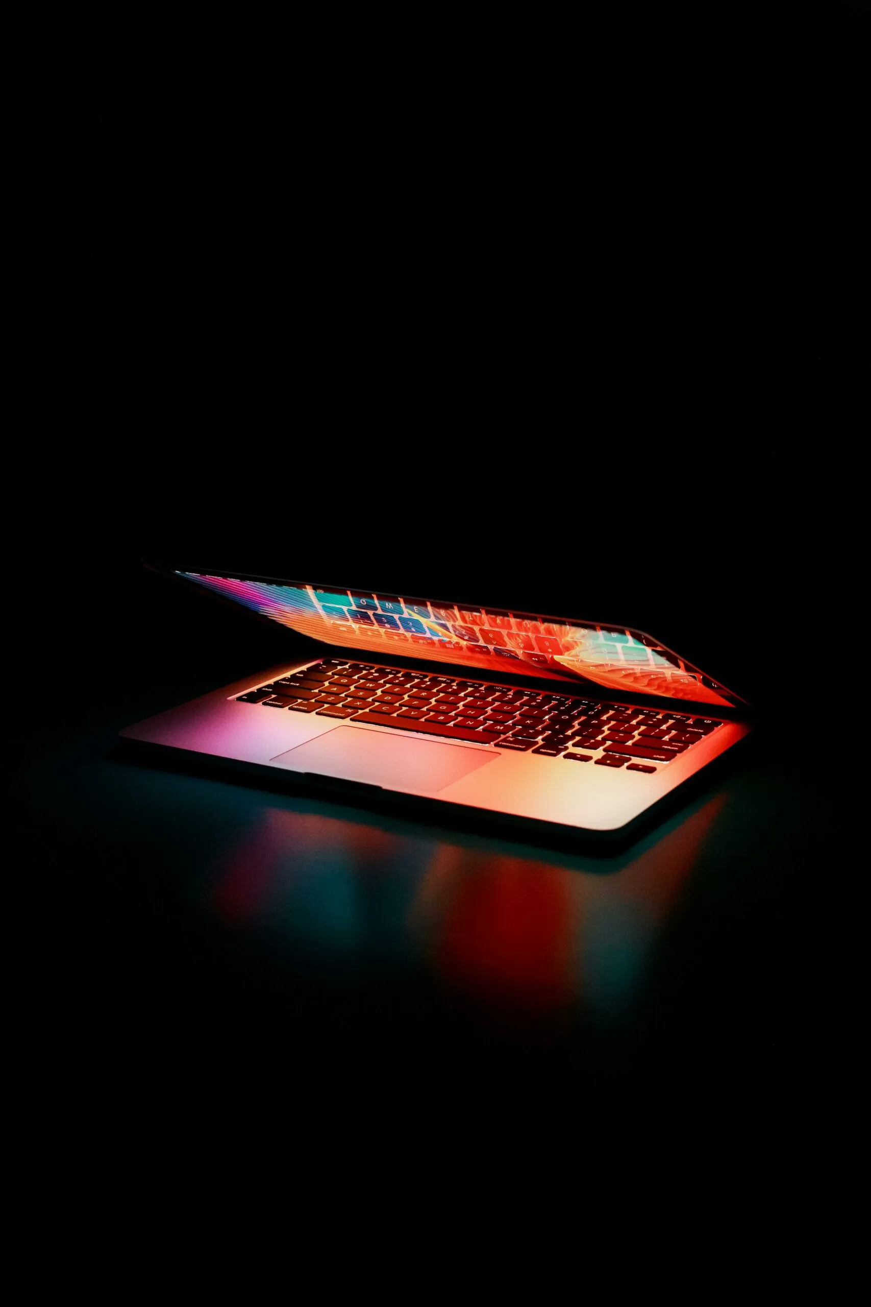 Ordinateur portable à moitié ouvert illuminé par des lumières colorées dans l’obscurité.