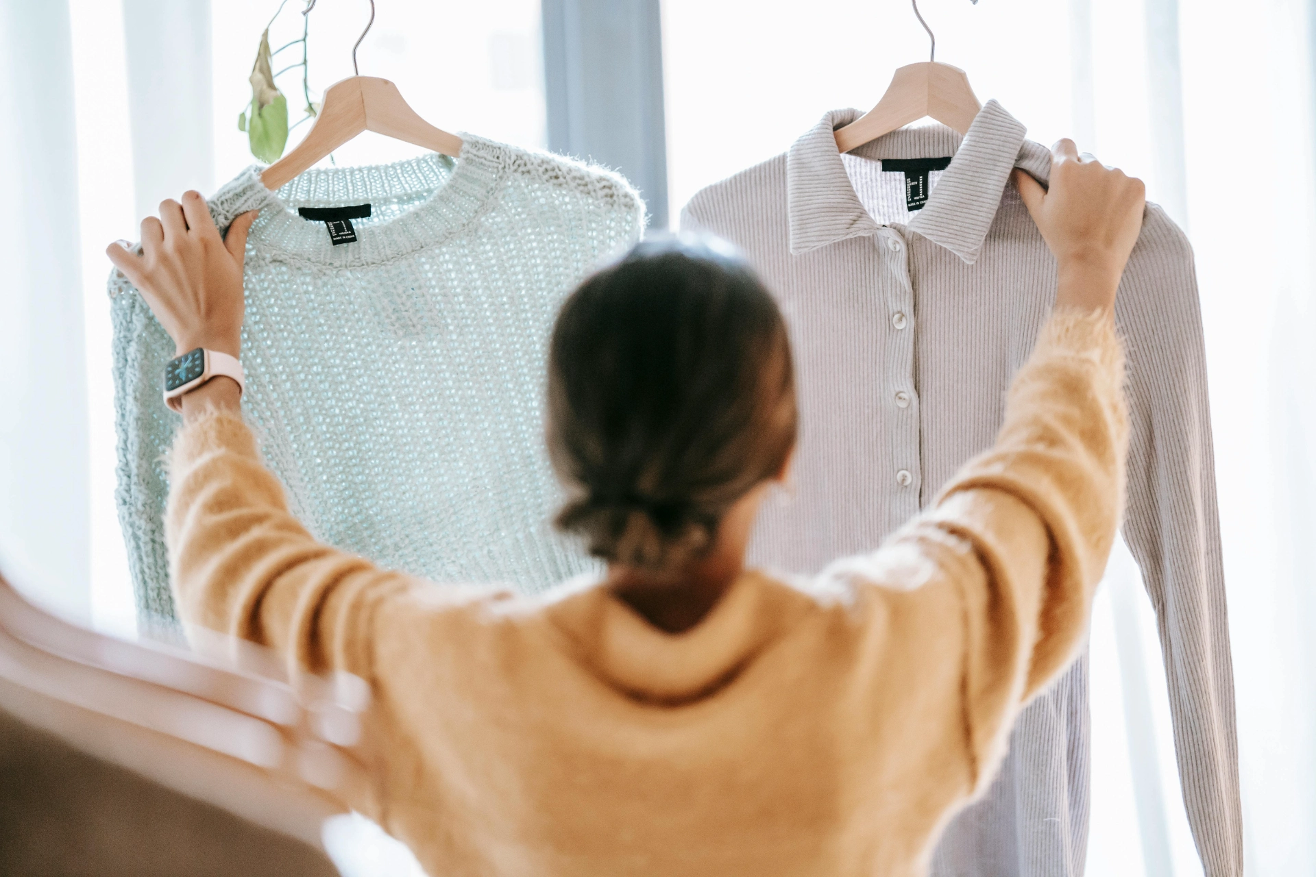 Une personne comparant deux vêtements accrochés sur des cintres pour choisir lequel porter.