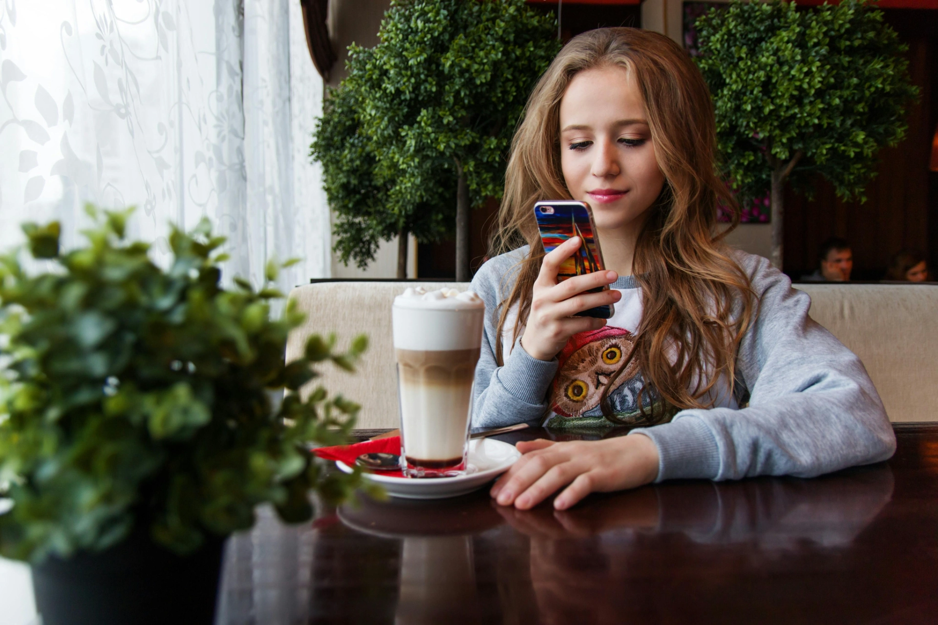 Jeune femme regardant son smartphone en buvant un café dans un café cosy.