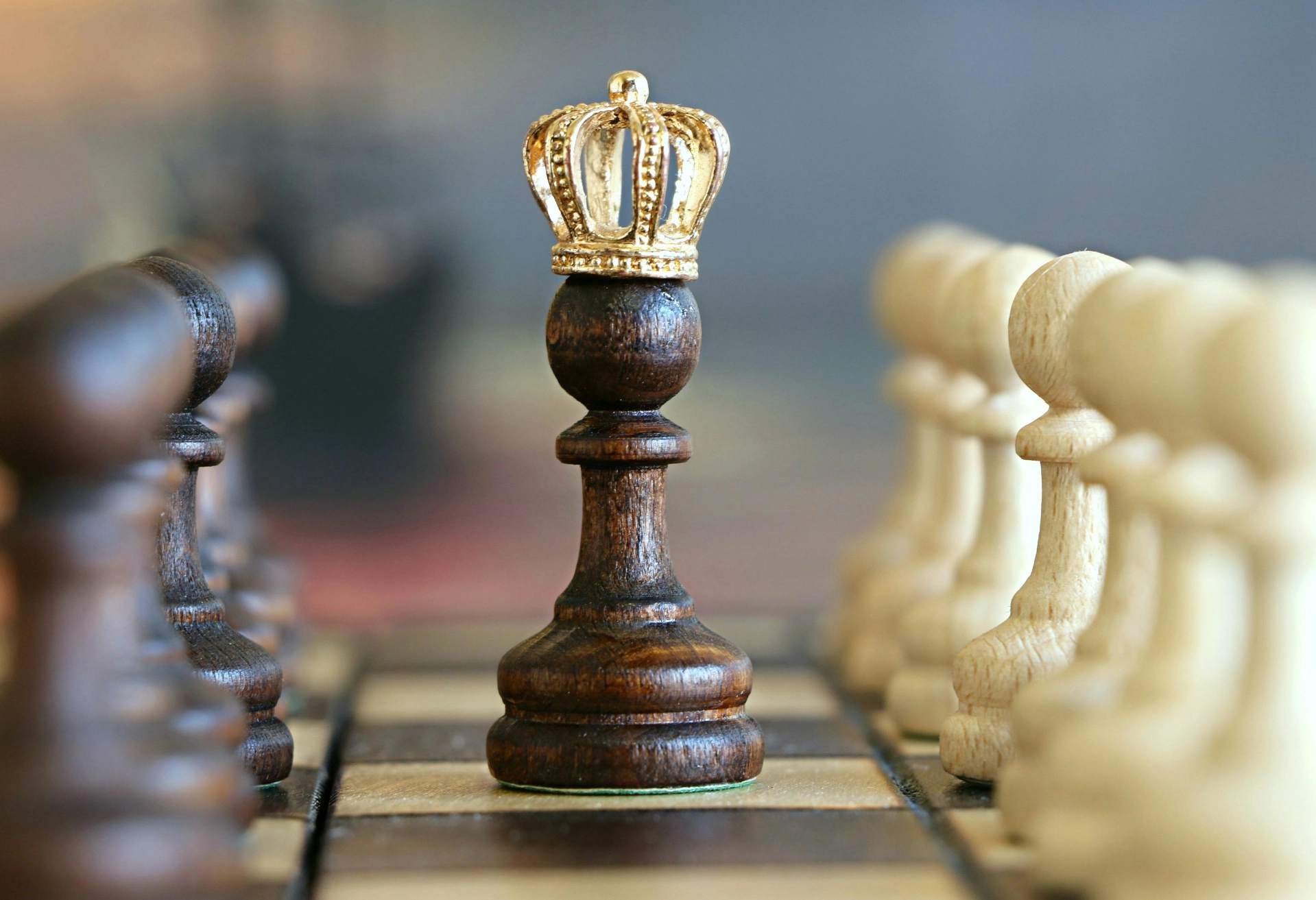 Pion d’échecs en bois foncé coiffé d’une couronne dorée sur un échiquier.