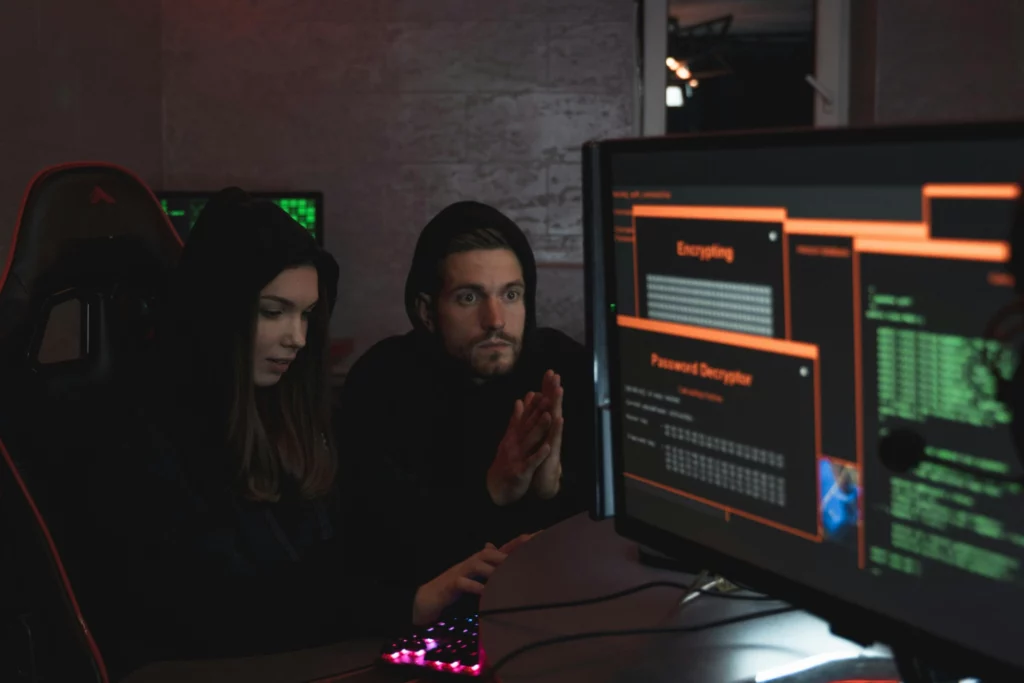 Deux hackers en sweat à capuche travaillant sur un ordinateur avec des écrans affichant un décryptage de mot de passe.