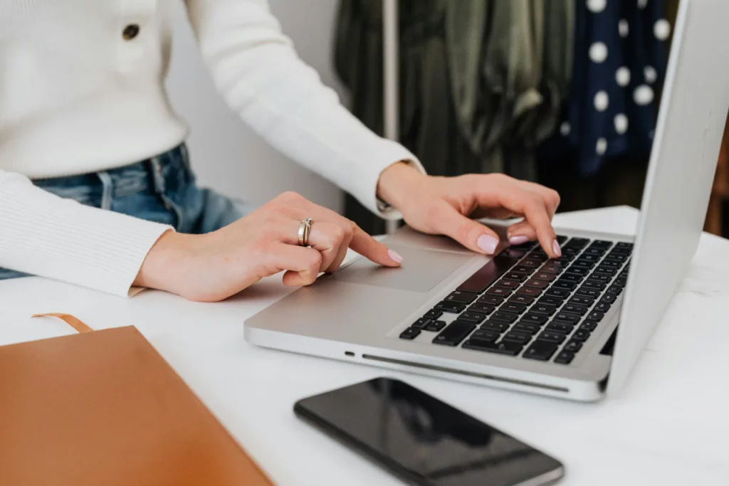 Femme utilisant un ordinateur portable sur une table avec un smartphone à proximité.