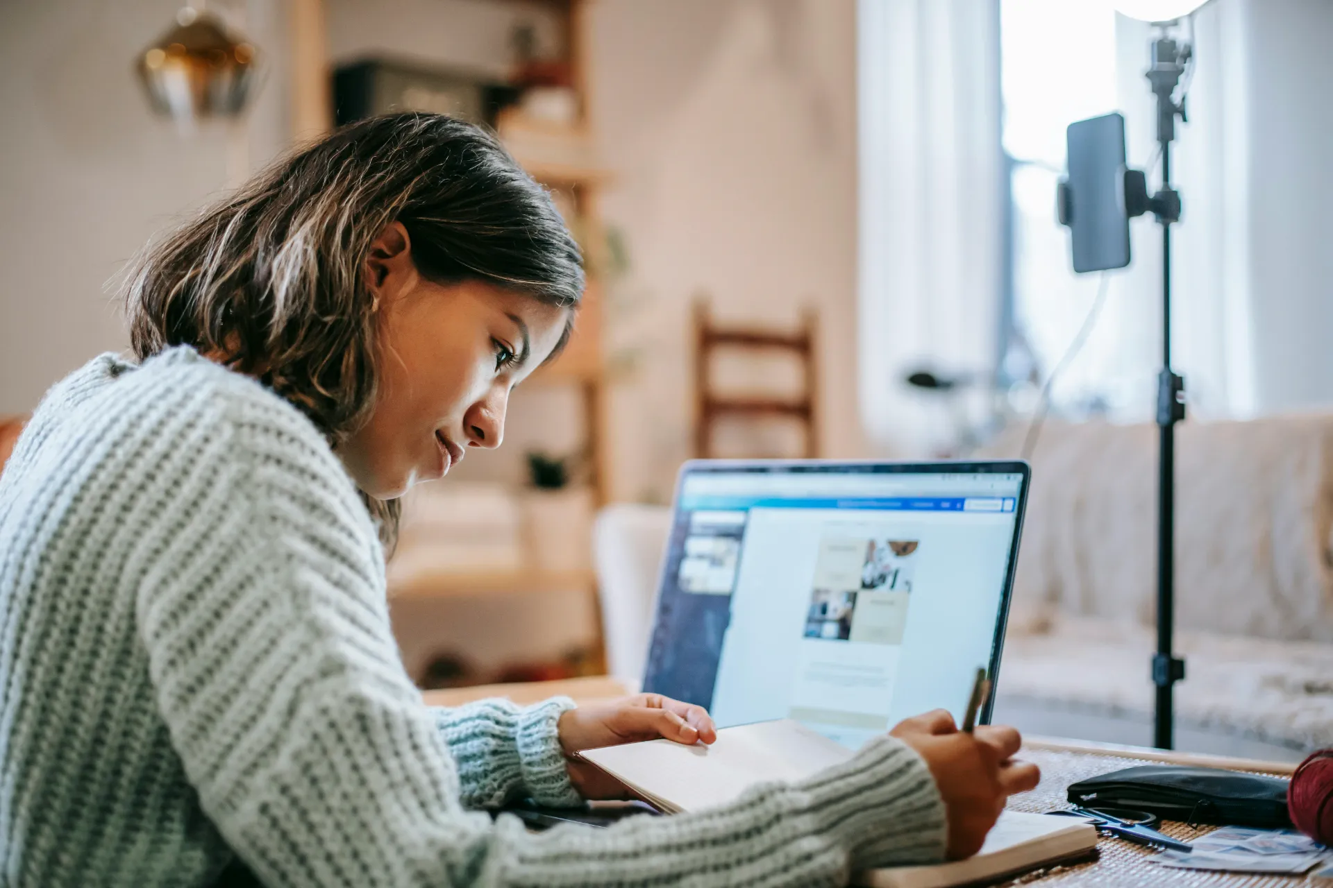 Jeune femme prenant des notes en consultant un site web sur son ordinateur portable.
