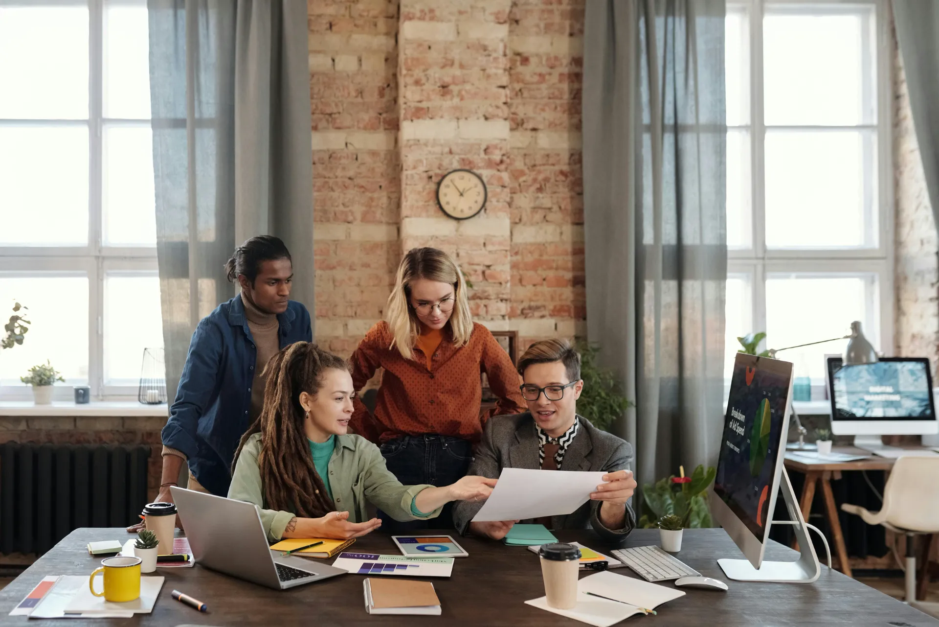 Équipe de jeunes professionnels collaborant autour de documents et d’ordinateurs dans un bureau moderne.