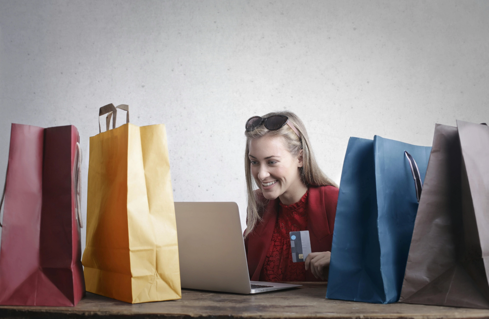 Femme souriante faisant du shopping en ligne avec une carte bancaire, entourée de sacs d’achats.
