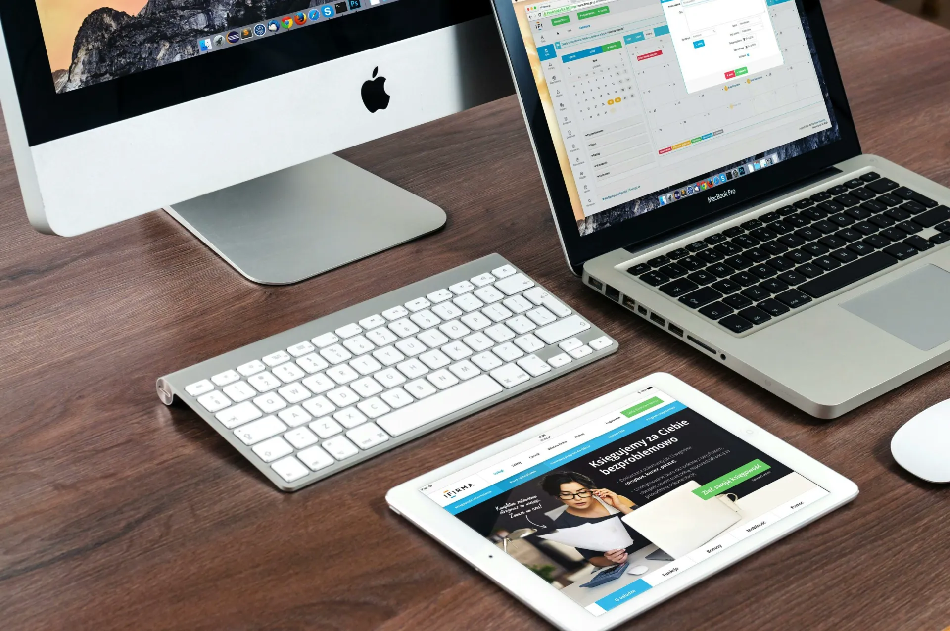Ordinateur de bureau, MacBook et tablette affichant des interfaces de gestion de projet sur un bureau en bois.