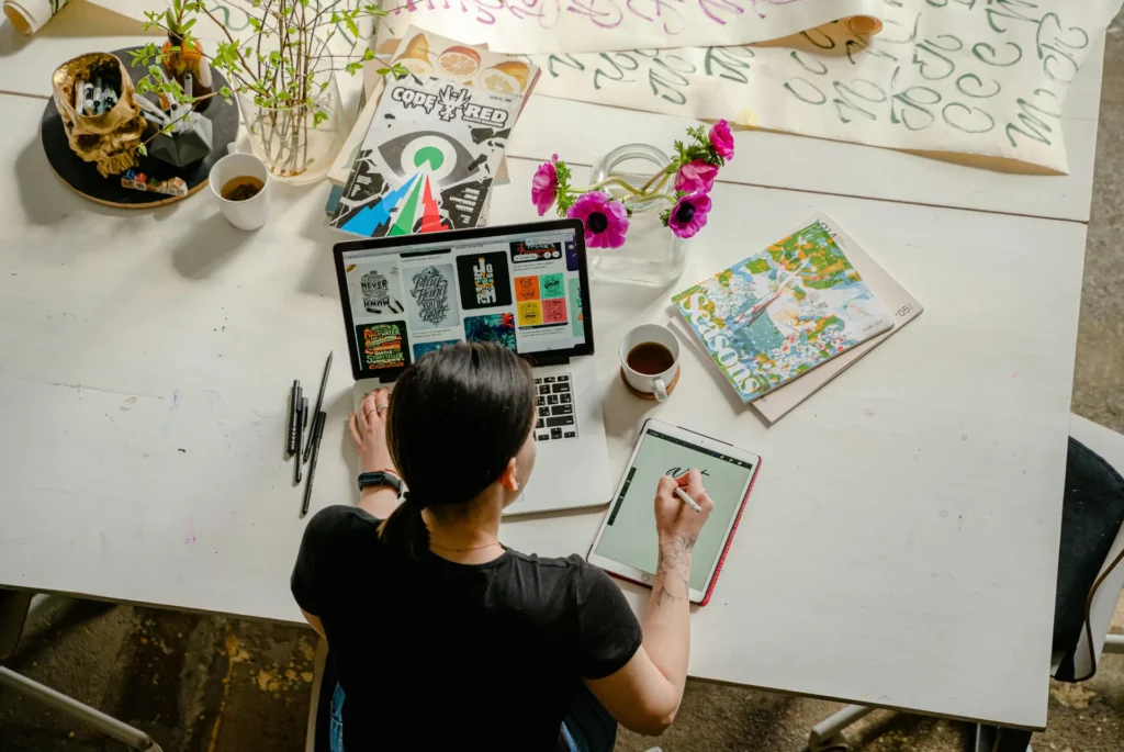 Designer travaillant sur une tablette graphique et un ordinateur portable dans un environnement créatif.