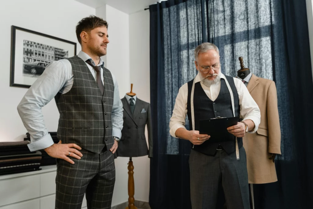 Un tailleur mesure un homme qui porte un costume sur-mesure dans un atelier de couture.