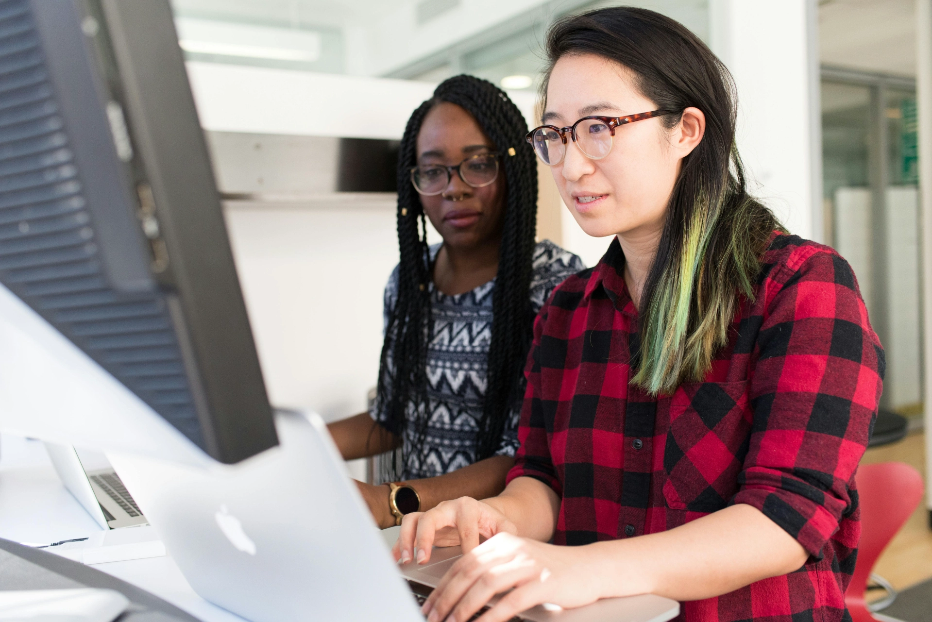 Deux femmes travaillant ensemble sur un ordinateur dans un bureau moderne.