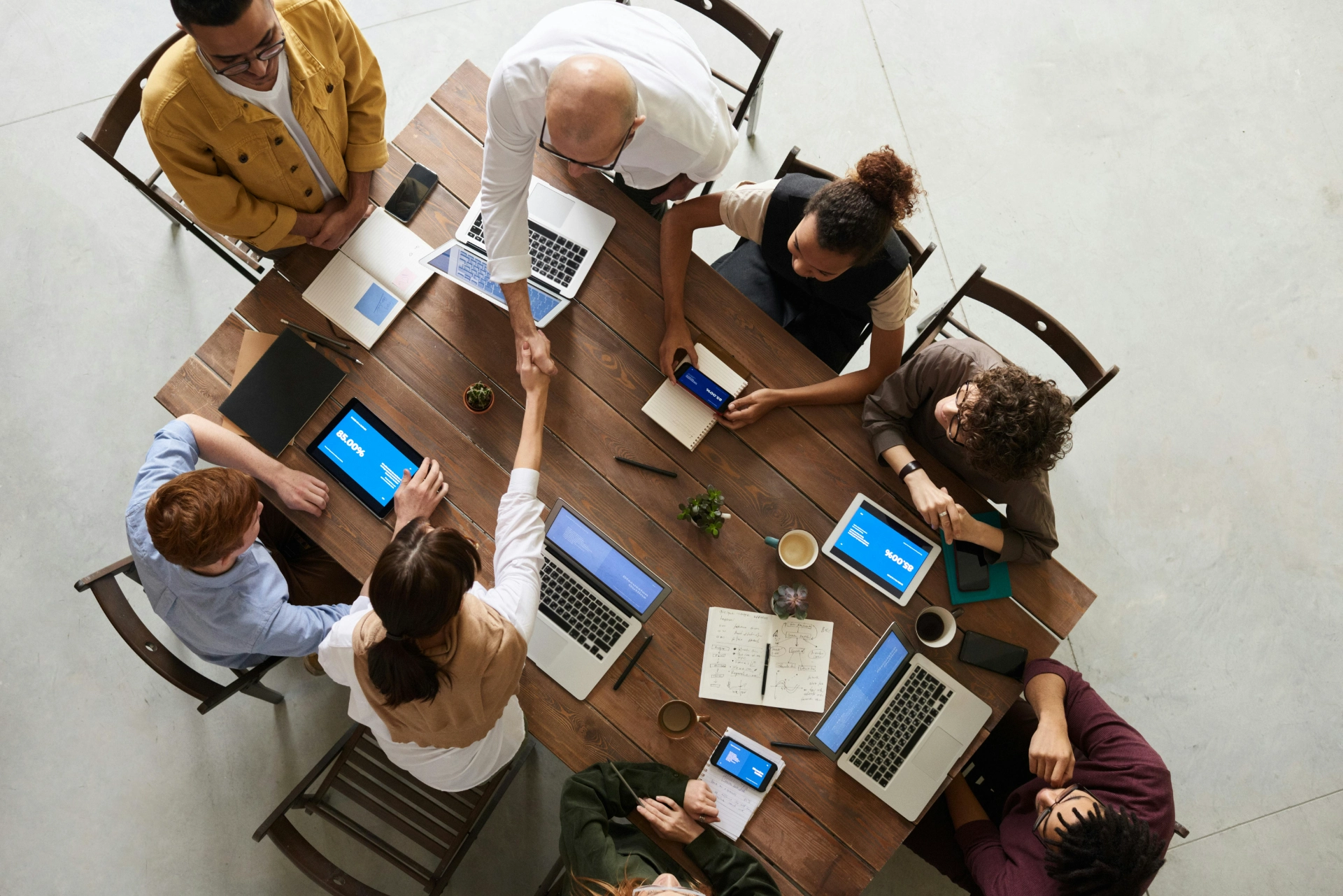 Vue de dessus d’un groupe de personnes en réunion autour d’une grande table avec des ordinateurs portables et des tablettes.