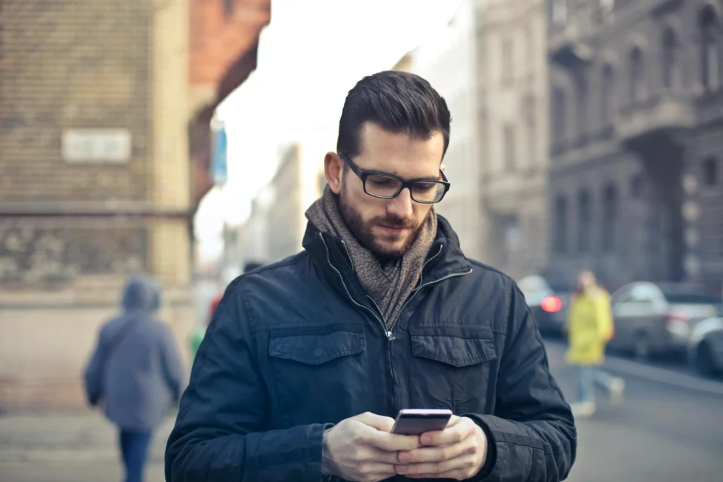 Homme avec des lunettes utilisant un smartphone en marchant en ville.