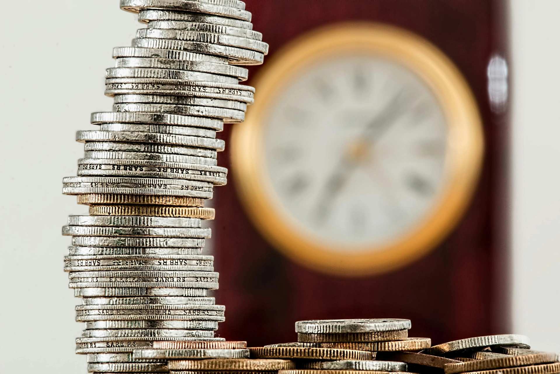 Pile de pièces de monnaie penchée avec une horloge floue en arrière-plan.