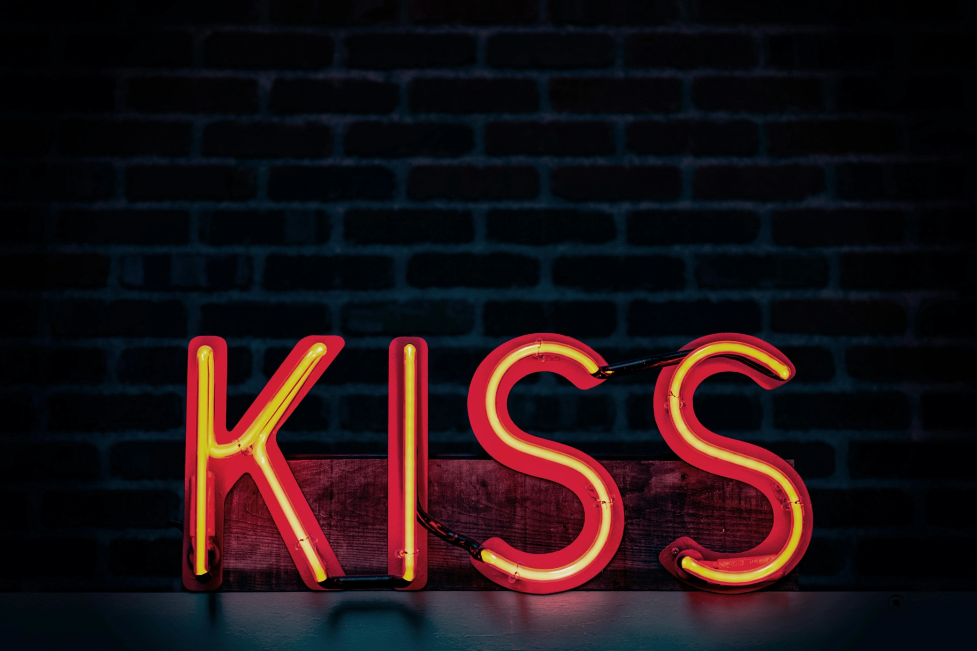 Signe au néon lumineux avec le mot "KISS" en rouge et jaune sur fond sombre de briques.